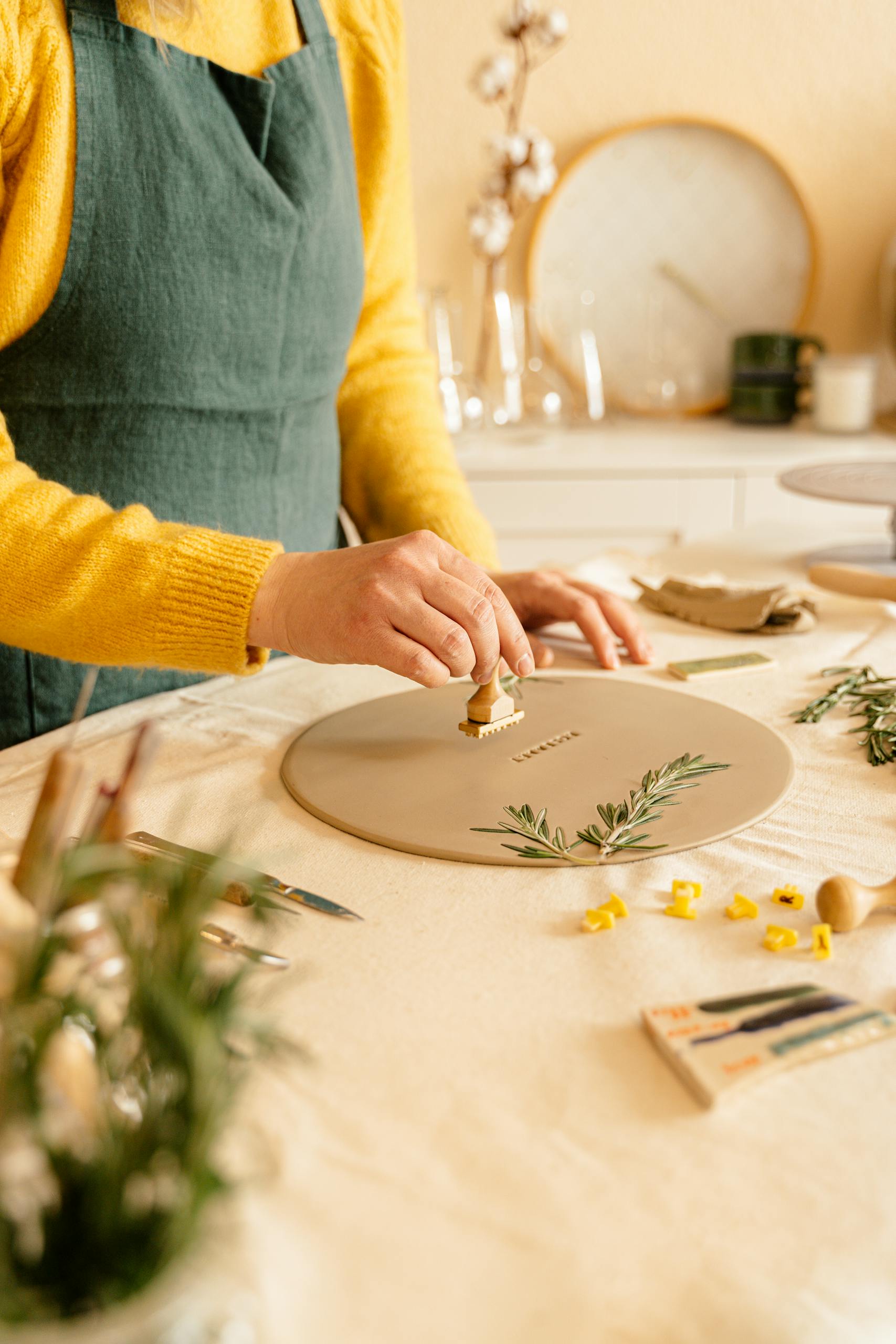 Person designing a ceramic plate using stamps and rosemary indoors. Les bienfaits des loisirs créatifs